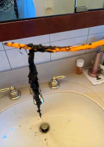 A bathroom sink with a clogged drain is shown. Black gunk is attached to an orange cleaning tool held above the sink