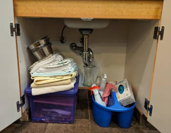 under sink with stack of towels and cleaners