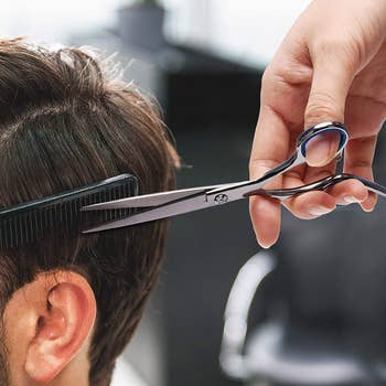hand holds silver shears and comb while trimming short dark hair