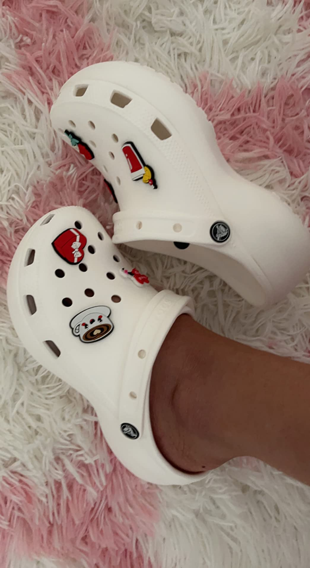White clogs with playful charms resting connected  a textured rug, showcasing a casual and amusive  footwear style