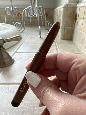 Hand holding a Laura Geller constitution  pencil successful  a bath  mounting  with tile antagonistic  and faucet disposable   successful  the background