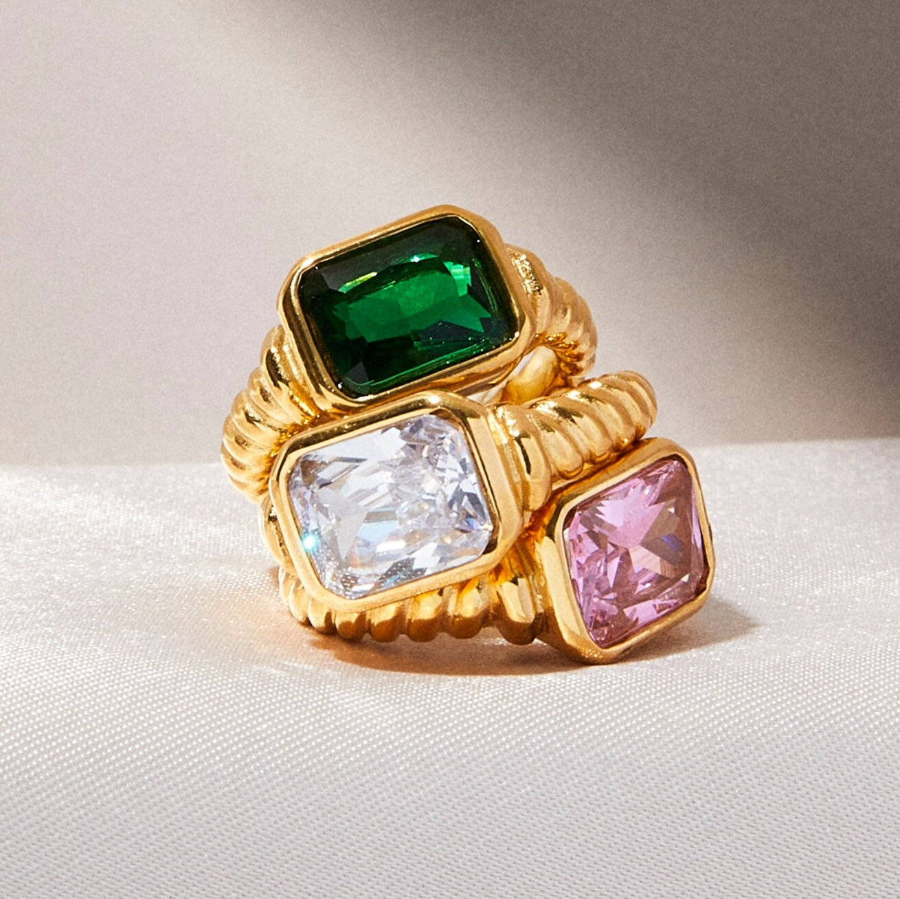 gold twist band rings with large stones in green, clear, and pink