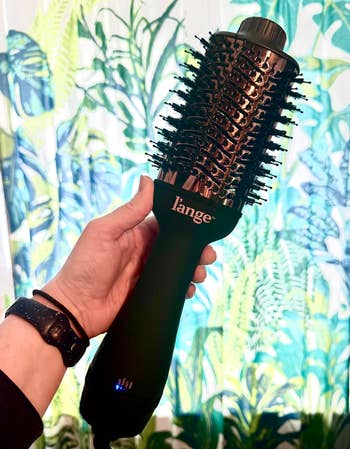 Person holding a large, round, achromatic  hairsbreadth  styling brushwood  with a marque  logo