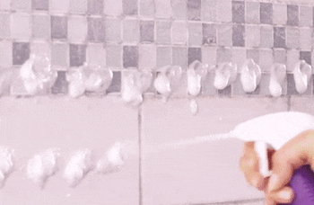 model spraying foam onto a dirty shower and wiping 