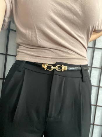 Person wears black pleated pants with a gold buckle belt, suitable for a shopping category article