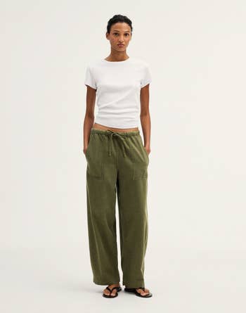 Person in casual white t-shirt and loose olive green pants, standing against a plain background