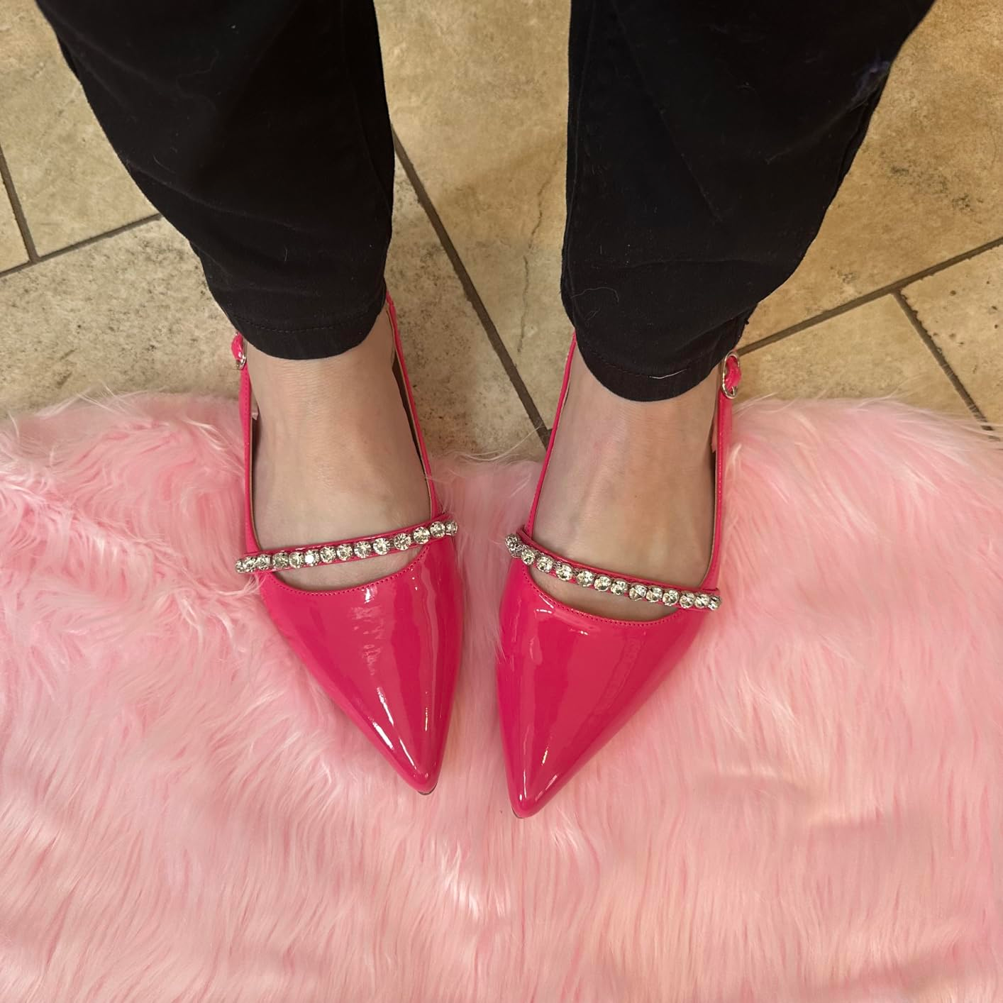 Person wearing shiny pointed shoes with rhinestone straps, lasting  connected  a pinkish  faux fur rug. Black pants are partially visible