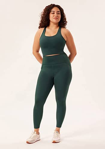 a model wearing the leggings in dark green with a matching bra  