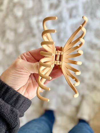 reviewer holding a large, beige butterfly-shaped hair clip with wide teeth, suitable for thick hair