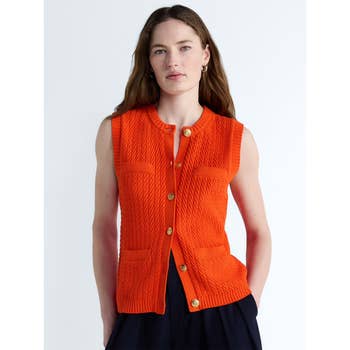 Person wearing a sleeveless, textured knit vest with gold buttons, paired with dark pants