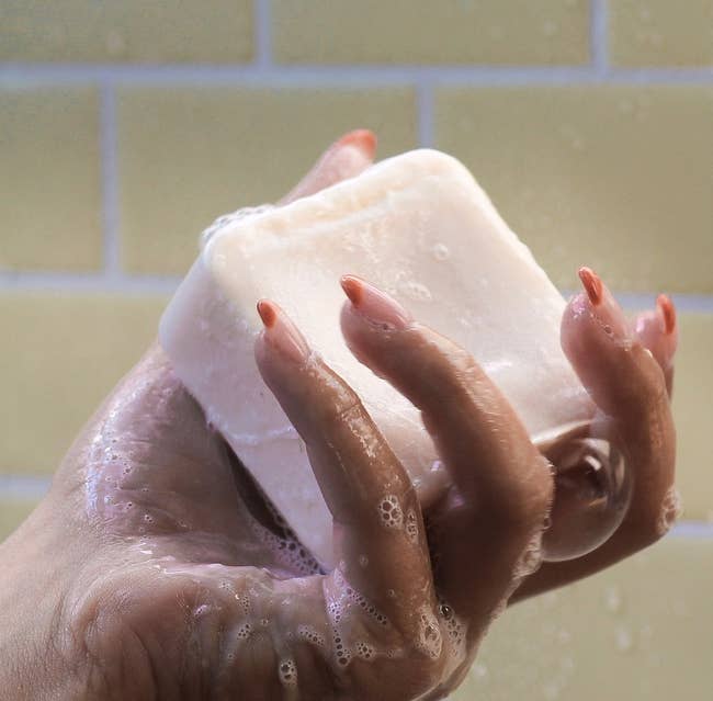 a hand holding a sudsy square shampoo bar 