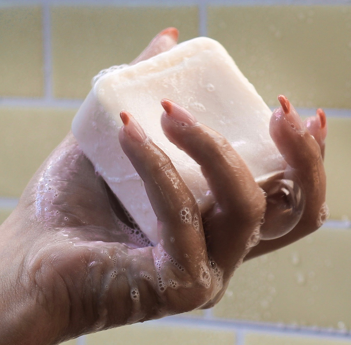 a hand holding a sudsy square shampoo bar
