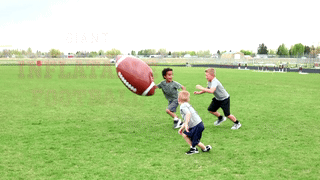 Three children play with giant inflatable football outdoors on a grassy field