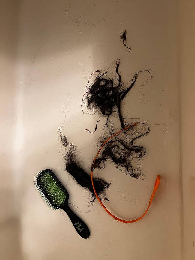 reviewer's orange drain snake with collected hair and hair brush for size comparison