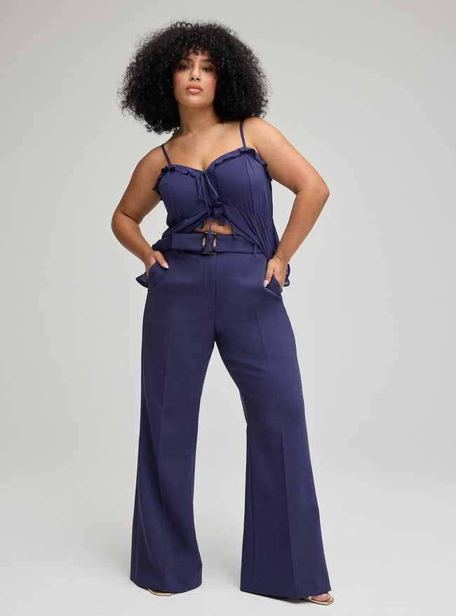 Person modeling wide-leg high-waisted pants and a sleeveless apical  with ruffle details, hands successful  pockets