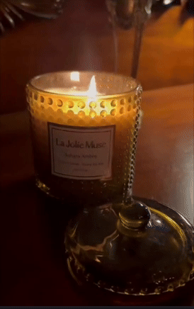 Lit candle successful  textured solid  jar with a decorative lid connected  a woody  surface. Label reads 