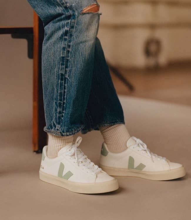model wearing white leather sneakers with a pale green suede V on them