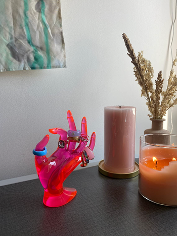Pink hand-shaped display mounted on a table with rings on its fingers 