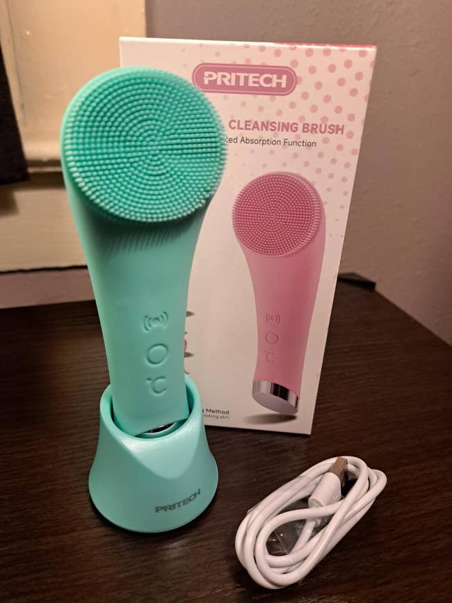 A facial cleansing brushwood  with a textured aboveground  is displayed adjacent  to its container  and a charging cable