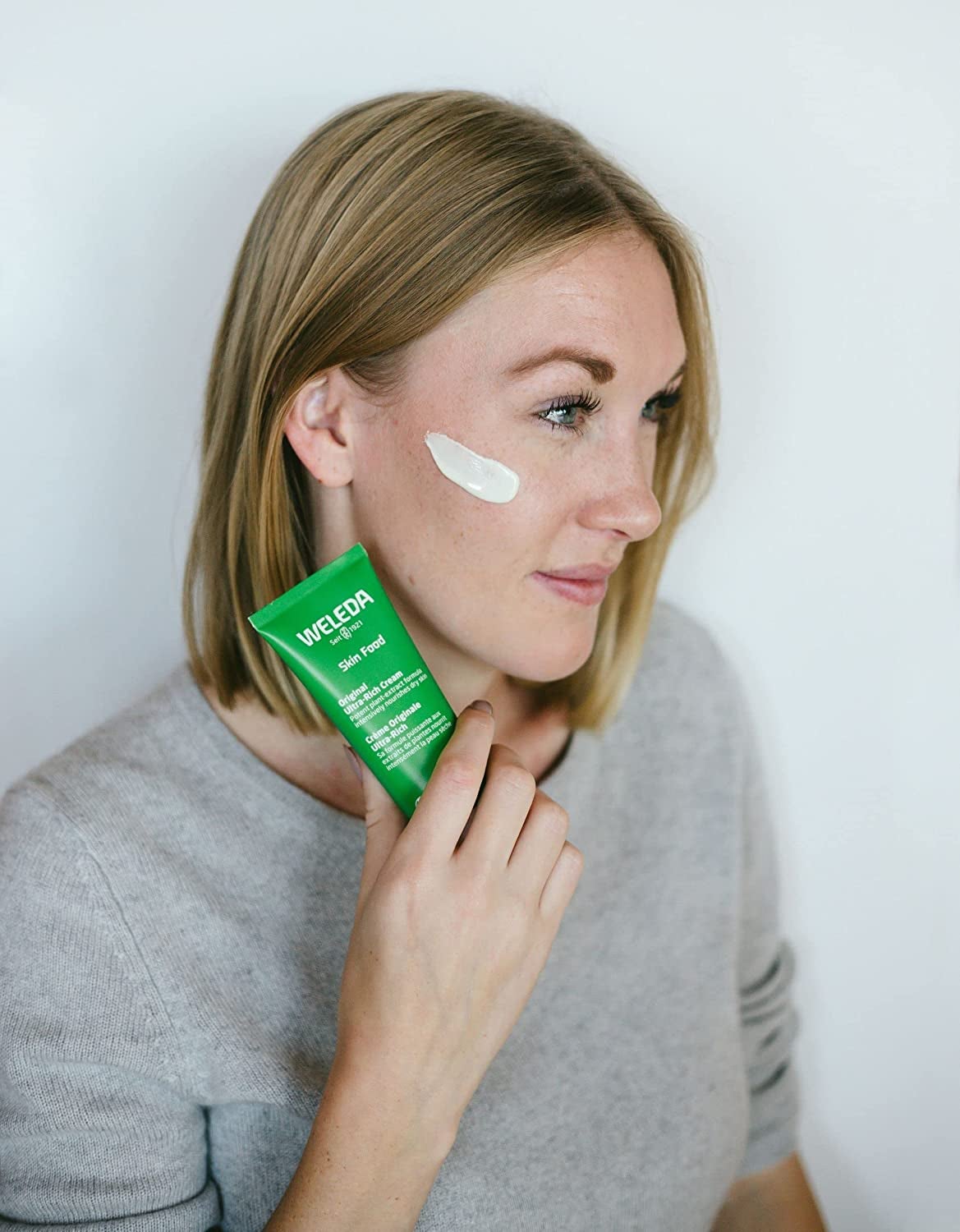 model holding the green tube next to her face with a swatched product