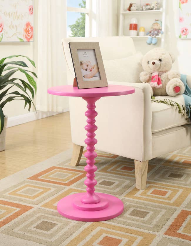 A circular topped hot pink end table with an abstract stem-like base 