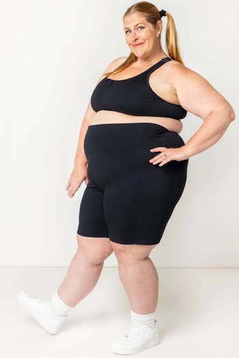 A positive size exemplary wearing a achromatic sports bra and shorts poses confidently successful achromatic sneakers, showcasing activewear