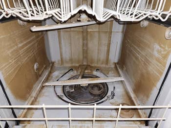 Interior view of a dirty dishwasher with racks and spray arms visible, 