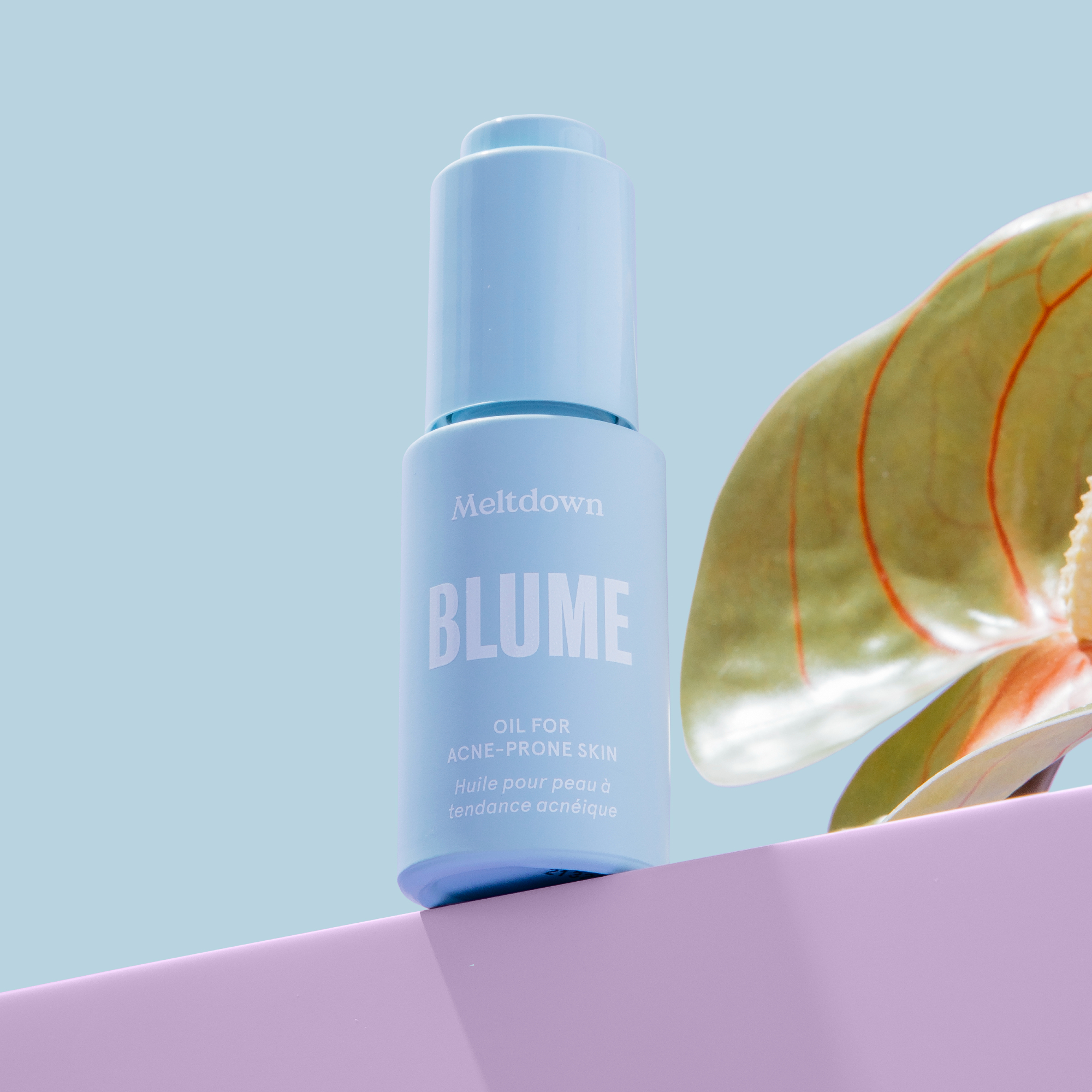 the blue bottle of face oil next to a plant