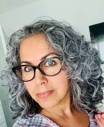 Person with curly hairsbreadth  and glasses, wearing a plaid top, looking astatine  the camera successful  a location  setting