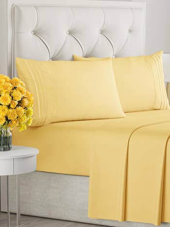 Yellow bedding set on a bed with a bouquet of flowers on the side table
