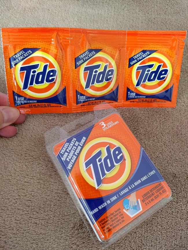 Three Tide travel sink packets above a Tide travel sink detergent box