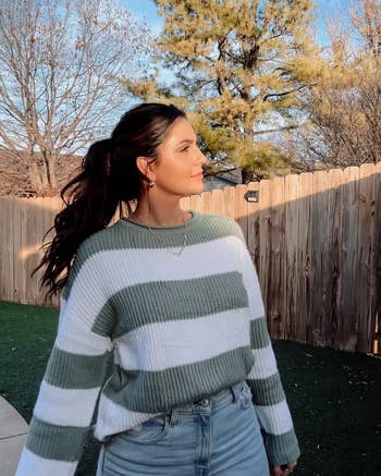Person outside, wearing a striped sweater and jeans, looking to the close successful a backyard setting. Clear skies and trees are disposable successful the background