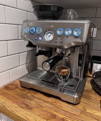 Reviewer photo of the espresso machine brewing a shot, with stainless steel design, on a kitchen counter