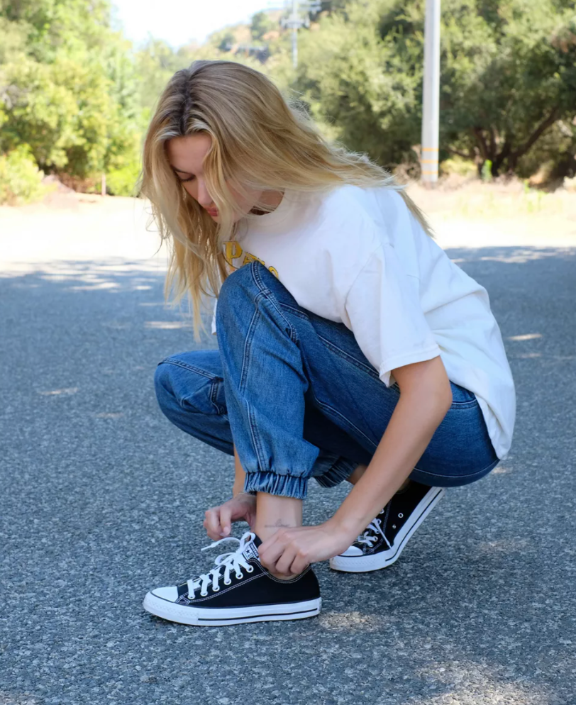 Model is crouching down reaching towards their black Converse shoes