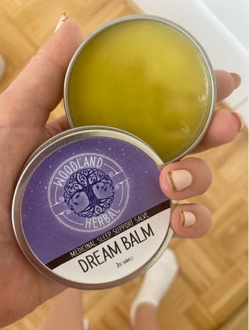 Dream balm in hand open to show the yellow balm inside 