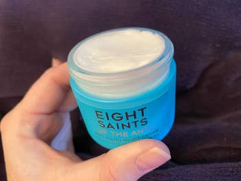 A manus  holding a jar of Eight Saints Up The Anti Anti Aging Night Cream with the lid open, revealing the pick  inside