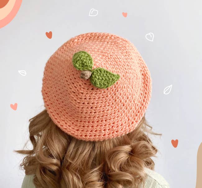 Model is wearing a peach colored crochet beret with a brown stem and two green leaves on the center