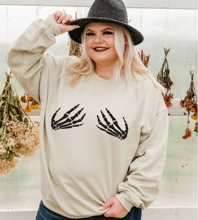 An ivory sweater with two black skeleton hands over the chest