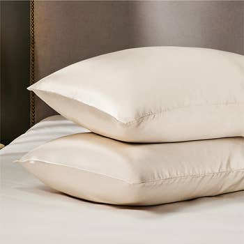 two pillows covered in cream-colored satin pillowcases on a bed