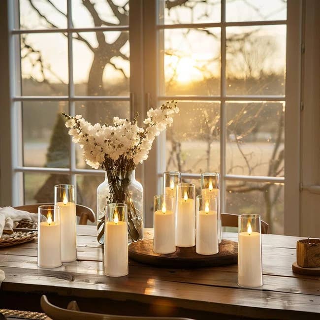 A dining table set with glowing pillar candles and a bouquet of flowers, framed by a window with a serene sunset view
