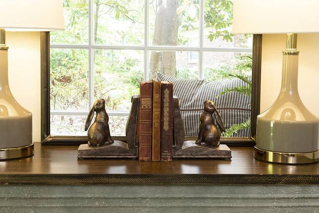 bookends that are rabbits sitting on open books holding up a stack of books
