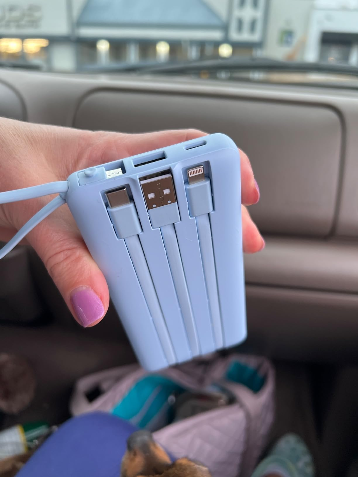 A hand holds a portable multi-charger with built-in connectors, ideal for travel and charging various devices