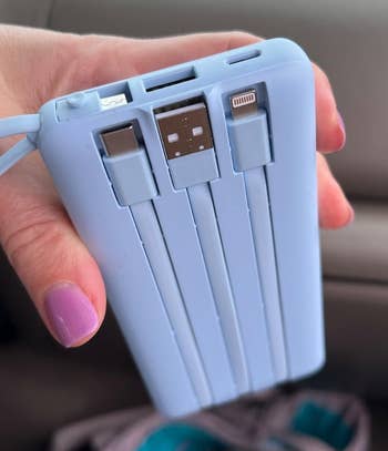 A hand holds a portable multi-charger with built-in connectors, ideal for travel and charging various devices