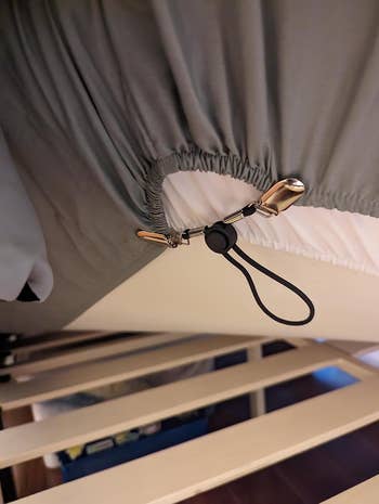 Sheet corner secured with an elastic clip to a bed frame, demonstrating a method to keep sheets in place