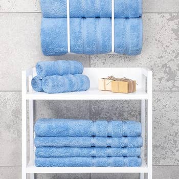 three rolled-up blue bath towels hanging above a stack of three blue washcloths in a bathroom