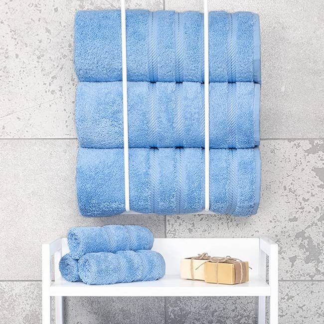 three rolled-up blue bath towels hanging above a stack of three blue washcloths in a bathroom
