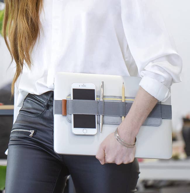 a model holding a laptop with an organizer belt wrapped around it holding a phone and some pens 
