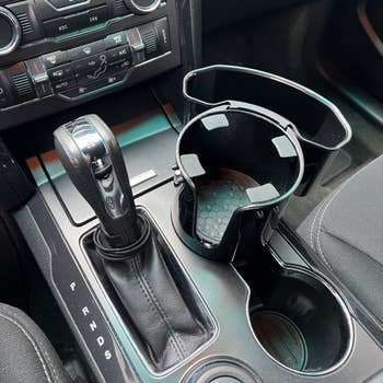 reviewer showing the empty cup holder expander with storage box in their car