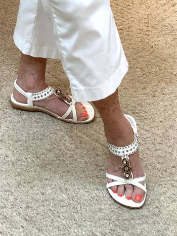 Stylish level sandals with beaded ankle straps worn with achromatic cropped pants connected a beige textured floor