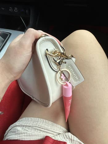 Person holding a tiny  decorator  handbag with a pinkish  articulator  gloss attached, seated successful  a car
